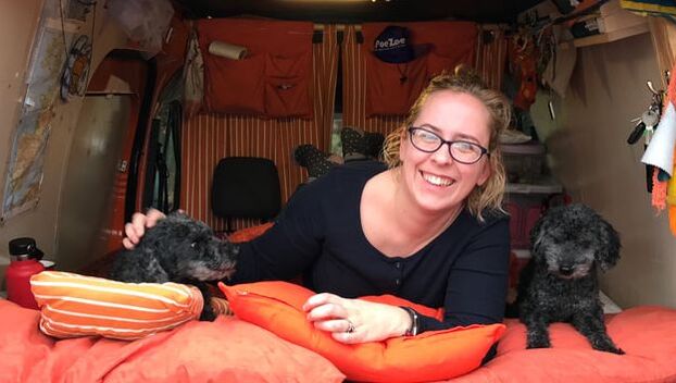 Rebecca lay in the back of an orange campervan laughing with two of her black toy poodles beside her.